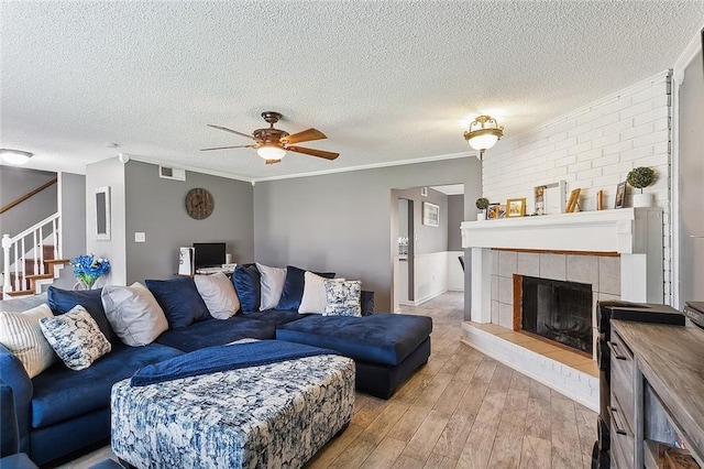 living room featuring a tiled fireplace, ornamental molding, a textured ceiling, and light hardwood / wood-style floors