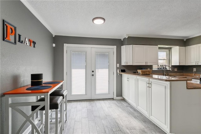 kitchen with white cabinetry, a textured ceiling, light hardwood / wood-style floors, and french doors