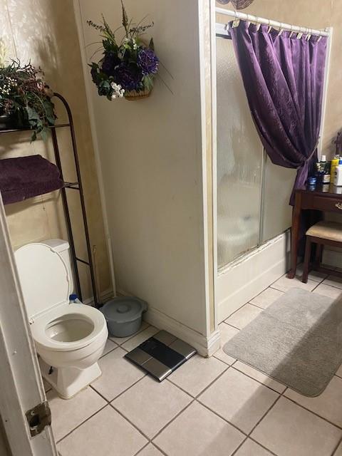 bathroom featuring toilet, tile patterned flooring, and combined bath / shower with glass door