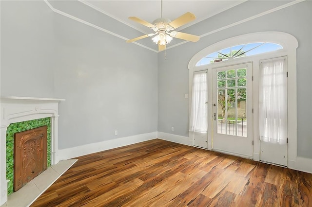 interior space with wood finished floors, a fireplace, crown molding, baseboards, and ceiling fan