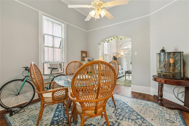 dining space with crown molding, ceiling fan, baseboards, wood finished floors, and arched walkways