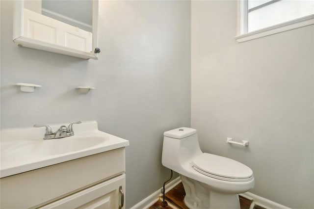 half bath featuring baseboards, toilet, wood finished floors, and vanity