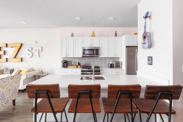 kitchen featuring appliances with stainless steel finishes, light hardwood / wood-style flooring, a breakfast bar area, and decorative backsplash