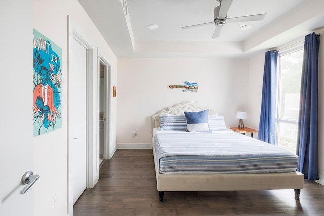 bedroom featuring ceiling fan, multiple windows, hardwood / wood-style flooring, and a raised ceiling