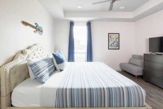 bedroom with hardwood / wood-style flooring, a raised ceiling, and ceiling fan