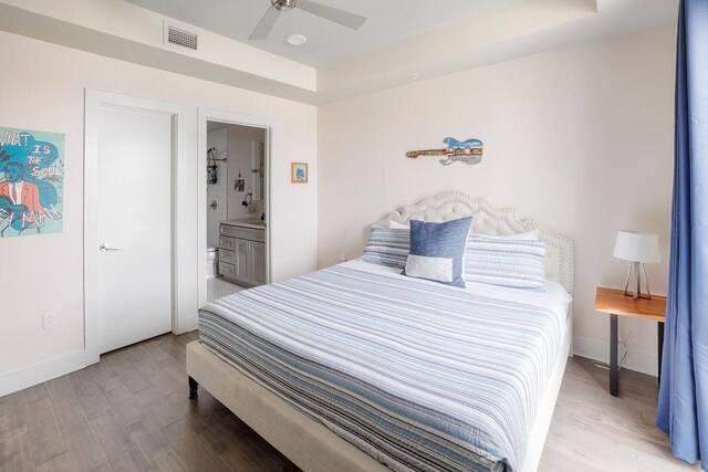 bedroom featuring ensuite bath, ceiling fan, a raised ceiling, and hardwood / wood-style floors