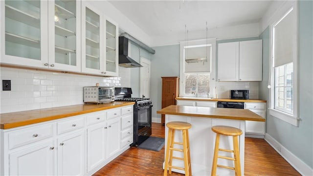 kitchen featuring butcher block countertops, white cabinetry, black appliances, a kitchen bar, and wall chimney exhaust hood