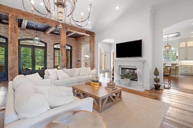 living room featuring french doors, brick wall, crown molding, a notable chandelier, and light hardwood / wood-style floors