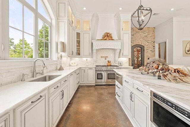 kitchen featuring premium range hood, range with two ovens, sink, decorative light fixtures, and white cabinetry