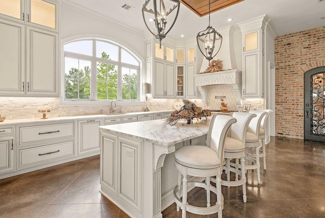 kitchen featuring light stone counters, custom range hood, sink, pendant lighting, and a kitchen island