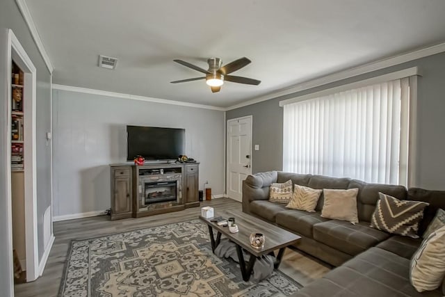 living room featuring a ceiling fan, baseboards, visible vents, light wood-style flooring, and ornamental molding