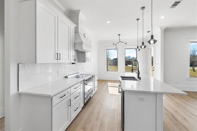 kitchen featuring high end stove, pendant lighting, an island with sink, sink, and light hardwood / wood-style floors