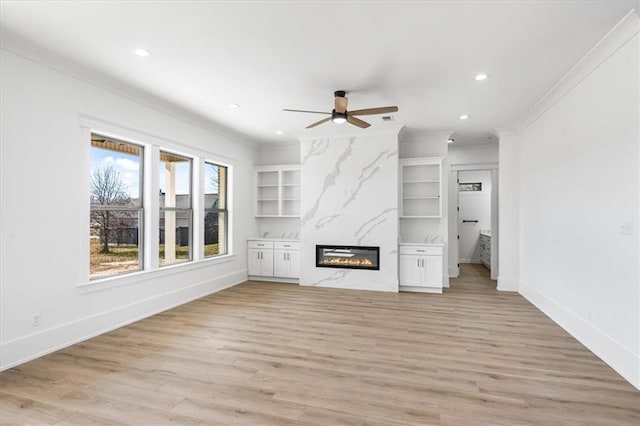 unfurnished living room with light wood-type flooring, built in features, ceiling fan, a fireplace, and ornamental molding