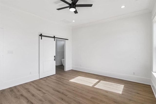 unfurnished bedroom featuring hardwood / wood-style flooring, ornamental molding, a barn door, and ceiling fan