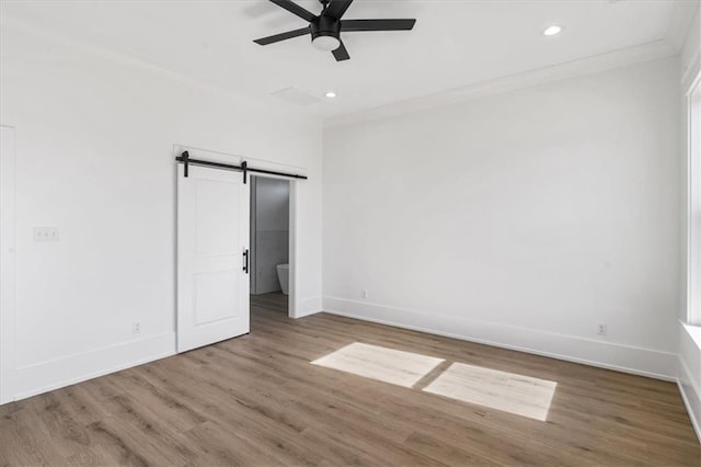 unfurnished bedroom featuring a barn door, ceiling fan, and hardwood / wood-style floors