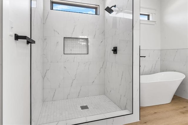 bathroom featuring independent shower and bath, a healthy amount of sunlight, hardwood / wood-style flooring, and tile walls