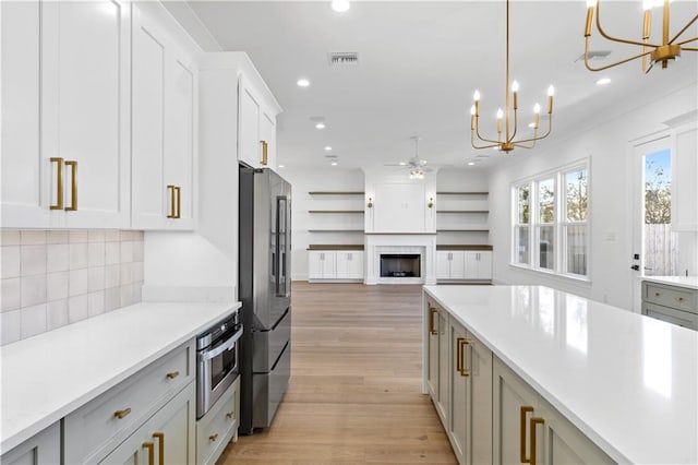 kitchen featuring decorative light fixtures, light hardwood / wood-style floors, ceiling fan with notable chandelier, stainless steel appliances, and tasteful backsplash