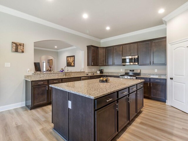 kitchen featuring light wood-type flooring, appliances with stainless steel finishes, dark brown cabinets, and a center island