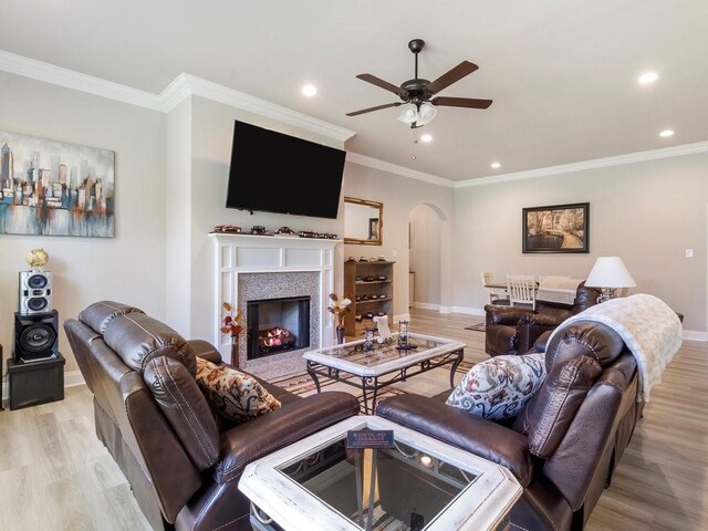 living area with light wood-type flooring, baseboards, arched walkways, and ornamental molding