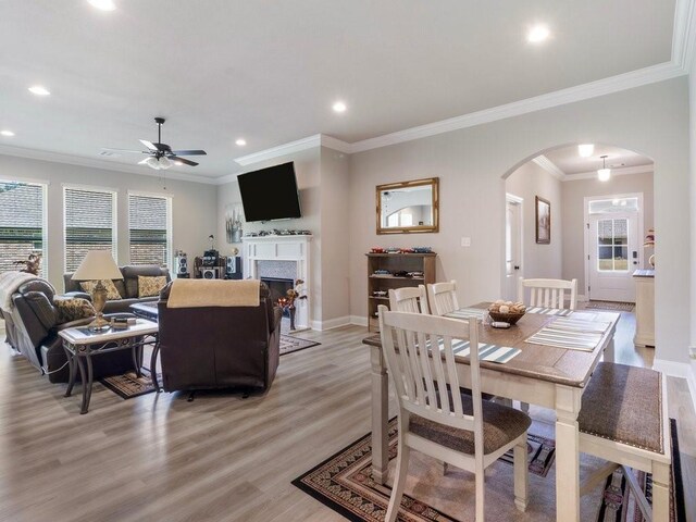 dining area featuring arched walkways, recessed lighting, light wood-type flooring, a warm lit fireplace, and baseboards