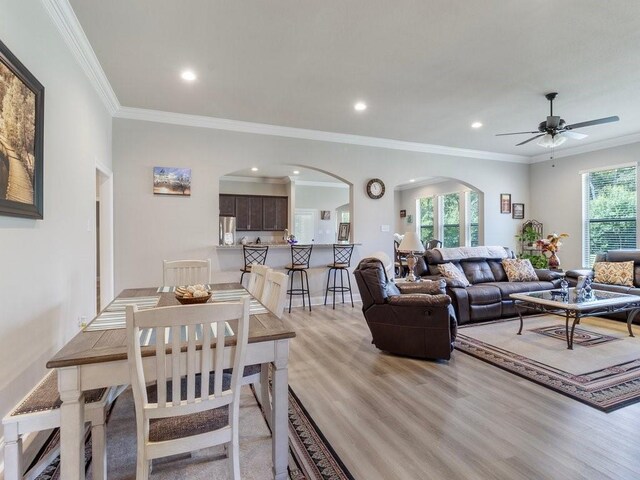 living area with arched walkways, recessed lighting, ornamental molding, ceiling fan, and light wood-type flooring