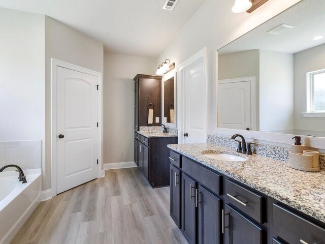 full bath with wood finished floors, two vanities, a sink, visible vents, and a bath