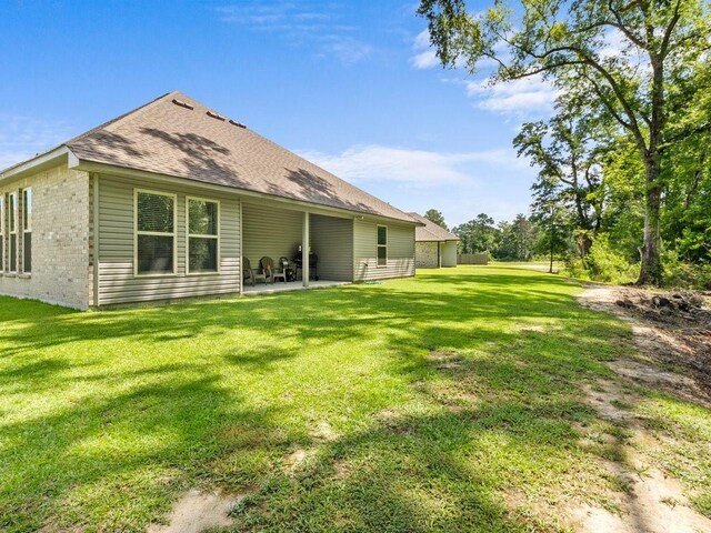 rear view of property featuring a patio area, a shingled roof, a lawn, and brick siding