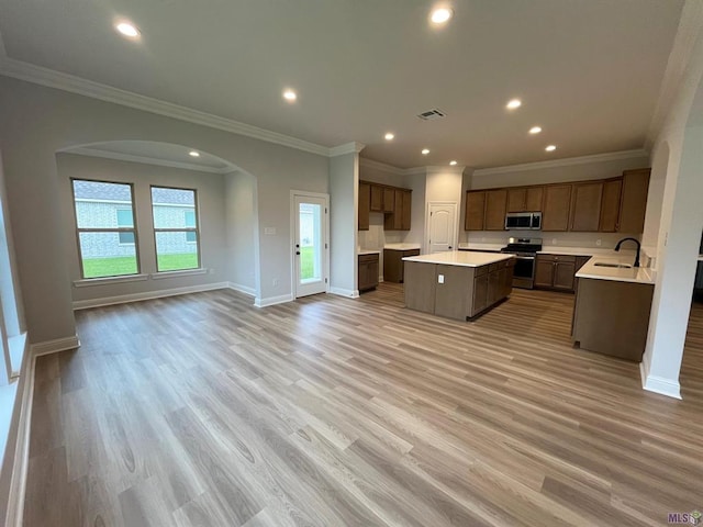 kitchen with light wood-type flooring, sink, a kitchen island, stainless steel appliances, and ornamental molding