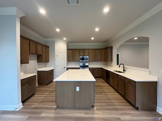 kitchen featuring ornamental molding, sink, a kitchen island, stainless steel appliances, and light wood-type flooring