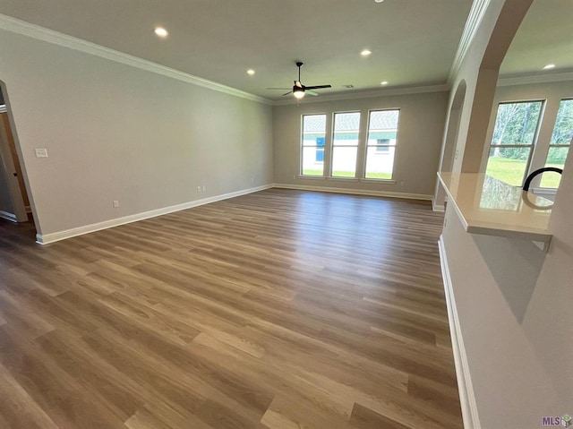 empty room with ceiling fan, crown molding, plenty of natural light, and wood-type flooring