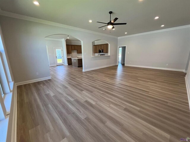 unfurnished living room featuring ornamental molding, a ceiling fan, arched walkways, and plenty of natural light