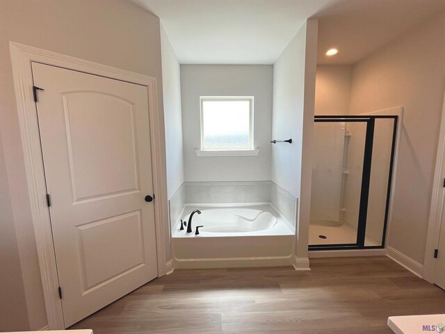 bathroom with baseboards, a stall shower, a garden tub, and wood finished floors