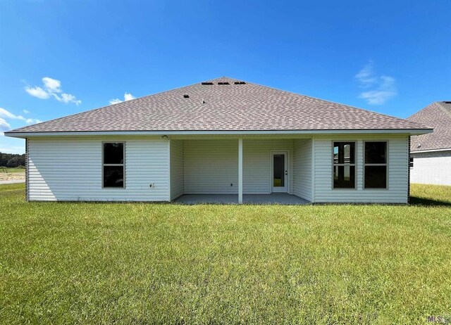back of house featuring a lawn, roof with shingles, and a patio