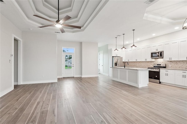 kitchen featuring appliances with stainless steel finishes, decorative light fixtures, white cabinets, a kitchen island with sink, and a raised ceiling