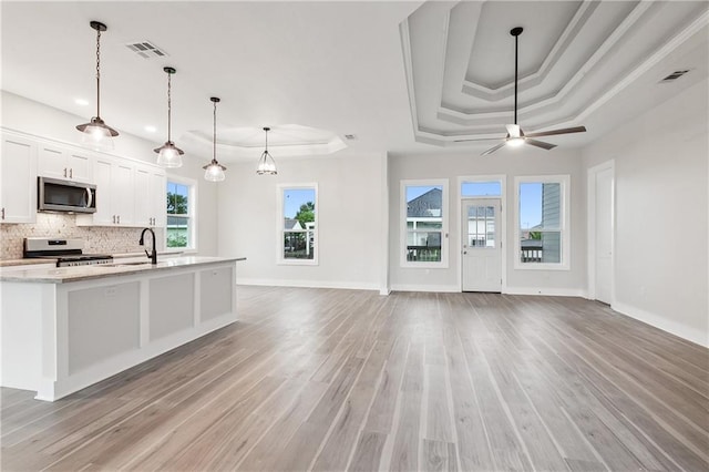 kitchen with decorative light fixtures, a raised ceiling, white cabinets, stainless steel appliances, and light stone countertops