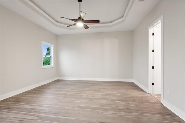 spare room featuring a raised ceiling, ceiling fan, and light hardwood / wood-style flooring