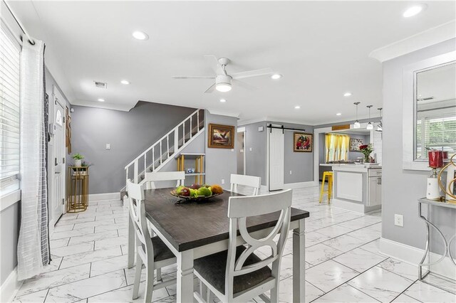 dining space with ceiling fan, a barn door, and ornamental molding