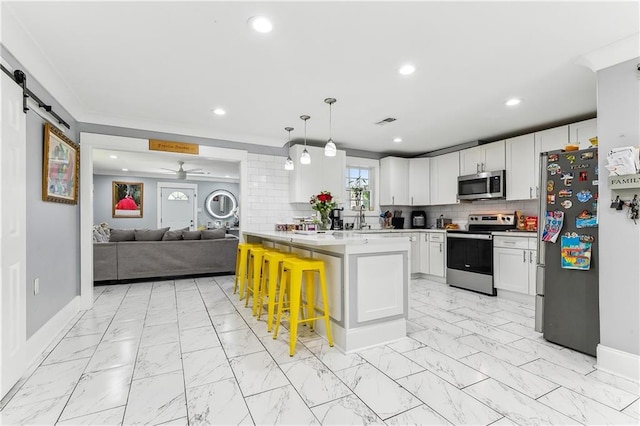 kitchen featuring a kitchen bar, hanging light fixtures, stainless steel appliances, a barn door, and white cabinets