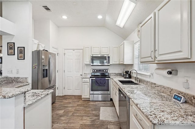 kitchen with white cabinetry, wood-type flooring, sink, appliances with stainless steel finishes, and lofted ceiling