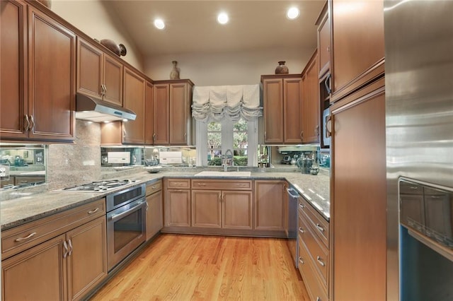 kitchen featuring lofted ceiling, light stone countertops, stainless steel appliances, light hardwood / wood-style floors, and sink