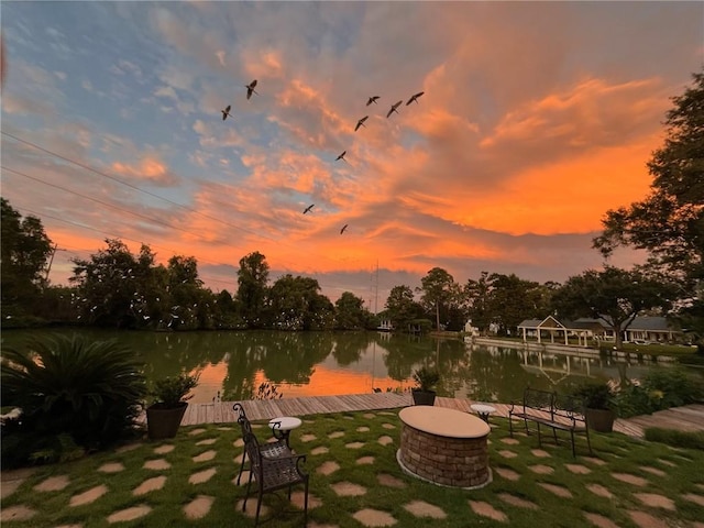 view of property's community featuring a boat dock, a fire pit, a lawn, and a water view