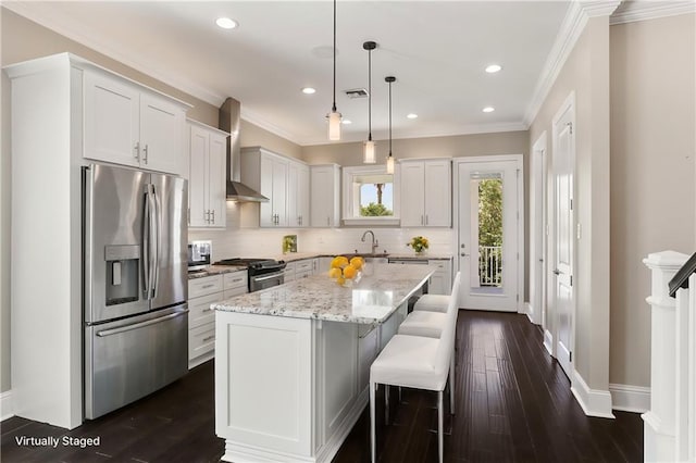 kitchen with appliances with stainless steel finishes, white cabinetry, dark wood-type flooring, wall chimney exhaust hood, and a kitchen island