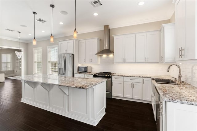 kitchen with wall chimney exhaust hood, a center island, appliances with stainless steel finishes, and white cabinetry