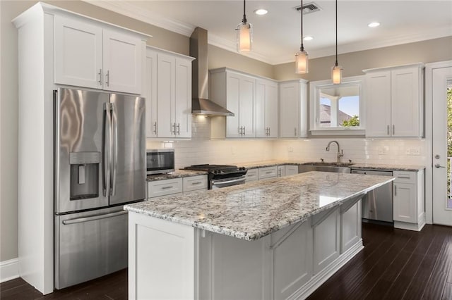 kitchen featuring visible vents, a kitchen island, wall chimney range hood, a sink, and appliances with stainless steel finishes