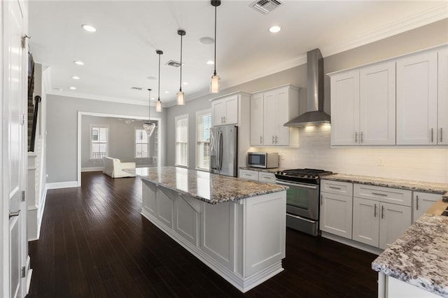 kitchen with wall chimney range hood, crown molding, appliances with stainless steel finishes, a center island, and visible vents