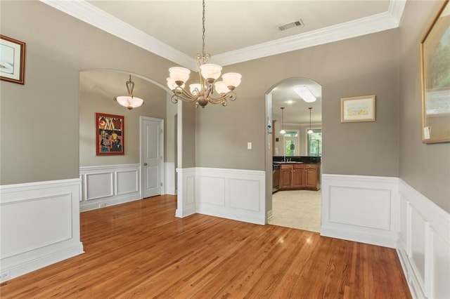 unfurnished dining area featuring wood-type flooring, crown molding, and an inviting chandelier