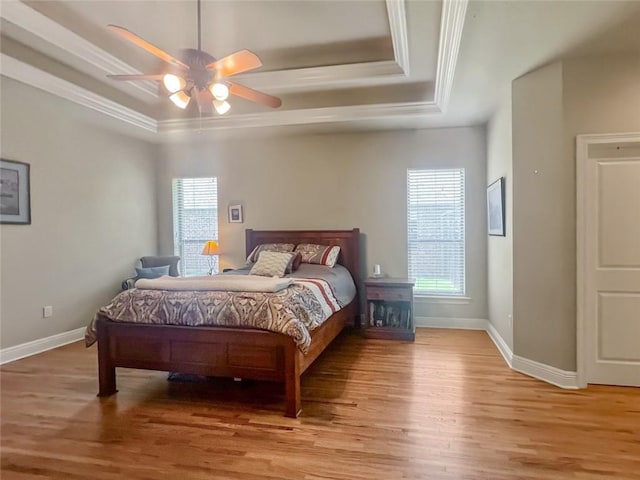 bedroom featuring ceiling fan, light hardwood / wood-style floors, a tray ceiling, and ornamental molding