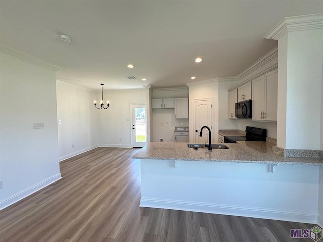 kitchen with a kitchen breakfast bar, dark wood-type flooring, kitchen peninsula, black appliances, and sink