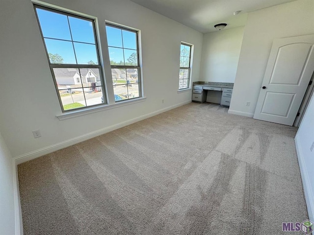 unfurnished bedroom with built in desk, light carpet, and multiple windows