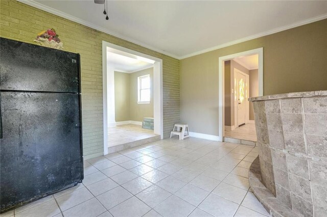 kitchen with black fridge, ceiling fan, brick wall, ornamental molding, and light tile patterned floors